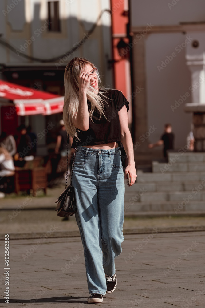 Stylish happy young woman walking down the street. Beautiful blonde girl portrait in the city. 