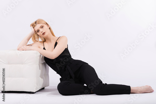 Portrait of a young and elegant girl who is sitting on the floor near the pouf on a white background.