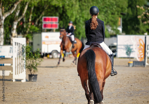 Rider with horse from behind in a show jumping tournament, out of focus in the background another participant galloping in the course.. © RD-Fotografie