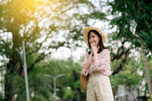 Portrait of asian young woman traveler with weaving hat and basket happy smile on green public park nature background. Journey trip lifestyle  world travel explorer or Asia summer tourism concept.
