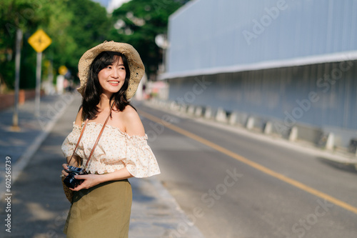 Portrait of asian young woman traveler with weaving hat and basket and a camera on green public park nature background. Journey trip lifestyle, world travel explorer or Asia summer tourism concept. © Jirawatfoto