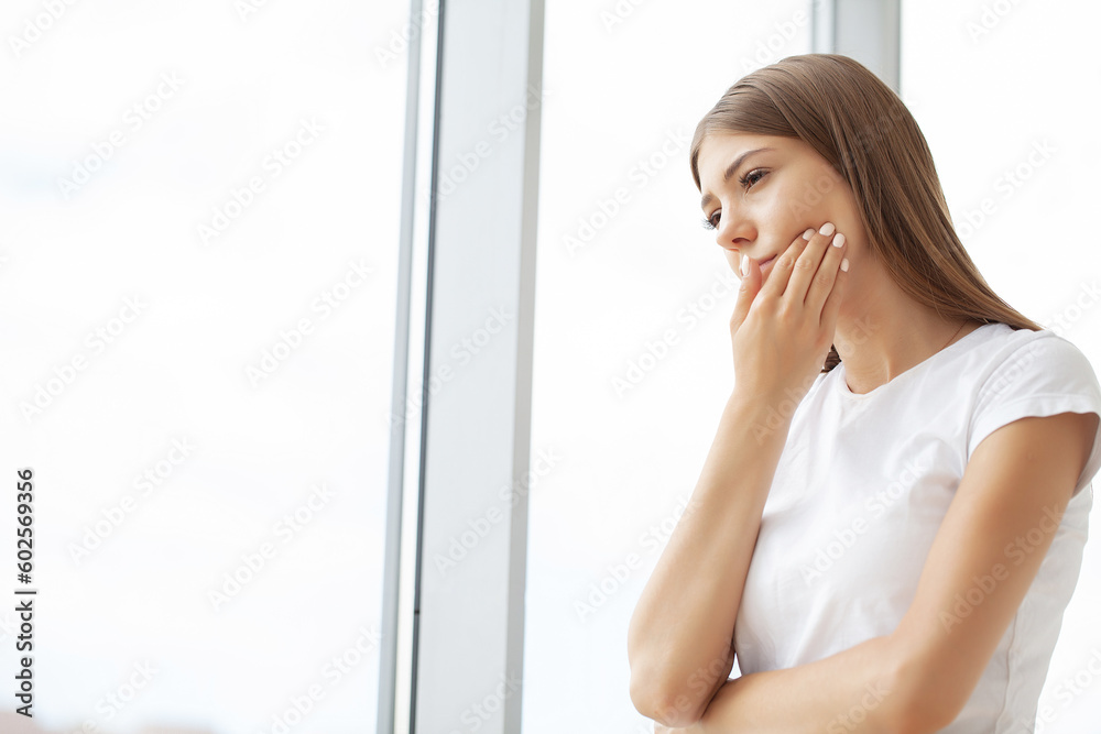 Woman suffering from toothache and touching her cheek while sitting at her desk