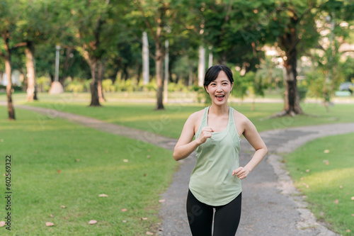 Fit young Asian woman jogging in park smiling happy running and enjoying a healthy outdoor lifestyle. Female jogger. Fitness runner girl in public park. healthy lifestyle and wellness being concept © Jirawatfoto