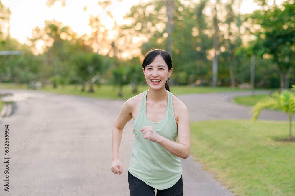 Fit Asian young woman jogging in park smiling happy running and enjoying a healthy outdoor lifestyle. Female jogger. Fitness runner girl in public park. healthy lifestyle and wellness being concept