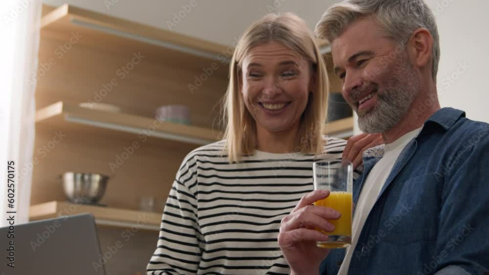 Caucasian adults man and woman middle-aged talking husband and wife family couple talk drink juice shopping online service booking travel tickets with laptop order food delivery discuss at kitchen Caucasian adults man and woman middle-aged talking husband and wife family couple talk drink juice shopping online service booking travel tickets with laptop order food delivery discuss at kitchen