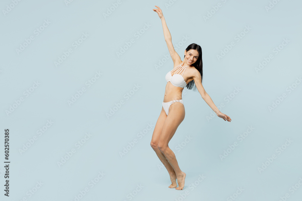 Full body young sexy woman wear swimsuit stand on toes raise up hands leaning back dance near hotel pool isolated on plain pastel light blue cyan background. Summer vacation sea rest sun tan concept.