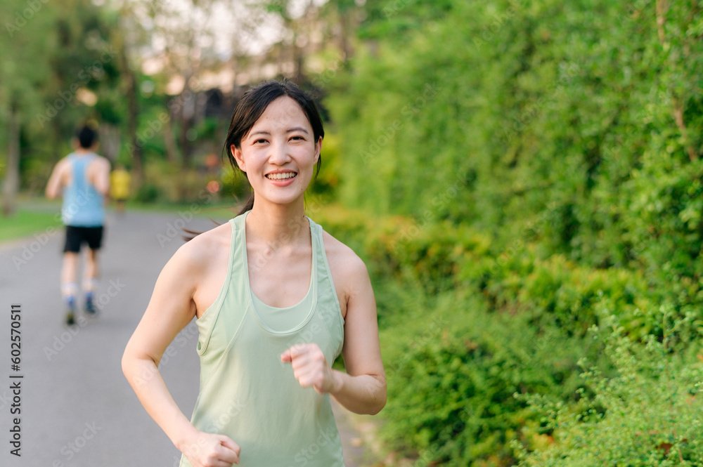 Fit Asian young woman jogging in park smiling happy running and enjoying a healthy outdoor lifestyle. Female jogger. Fitness runner girl in public park. healthy lifestyle and wellness being concept Fit Asian young woman jogging in park smiling happy running and enjoying a healthy outdoor lifestyle. Female jogger. Fitness runner girl in public park. healthy lifestyle and wellness being concept