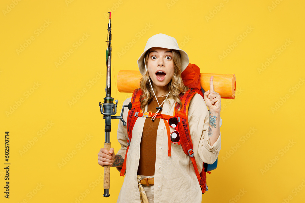 Young woman carry backpack with stuff mat hold fishing rod point finger up isolated on plain yellow background. Tourist leads active lifestyle walk on spare time. Hiking trek rest travel trip concept. Young woman carry backpack with stuff mat hold fishing rod point finger up isolated on plain yellow background. Tourist leads active lifestyle walk on spare time. Hiking trek rest travel trip concept.