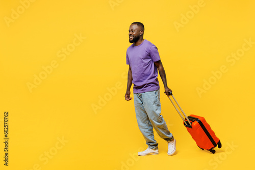 Traveler man wears casual clothes t-shirt hold suitcase go isolated on plain yellow background studio portrait. Tourist travel abroad in free spare time rest getaway. Air flight trip journey concept.