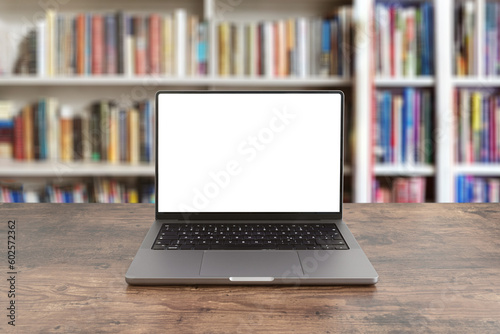 modern laptop computer with blank screen on wooden table against bookshelves filled with books