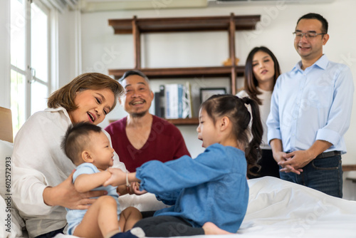 Portrait of happy love asian grandfather with grandmother playing with asian baby and little cute girl on bed.Big family love with their laughing grandparents smiling together.Family and togetherness