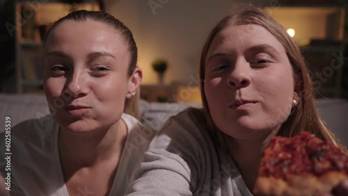 Closeup of two women eating pizza at night. Friends devouring unhealthy food.