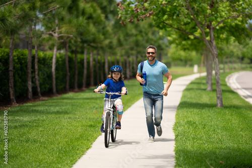 Little kid learning to ride bicycle with father in park. Father teaching son cycling. Father and son learning to ride a bicycle at Fathers day. Father support and helping son. Child care.