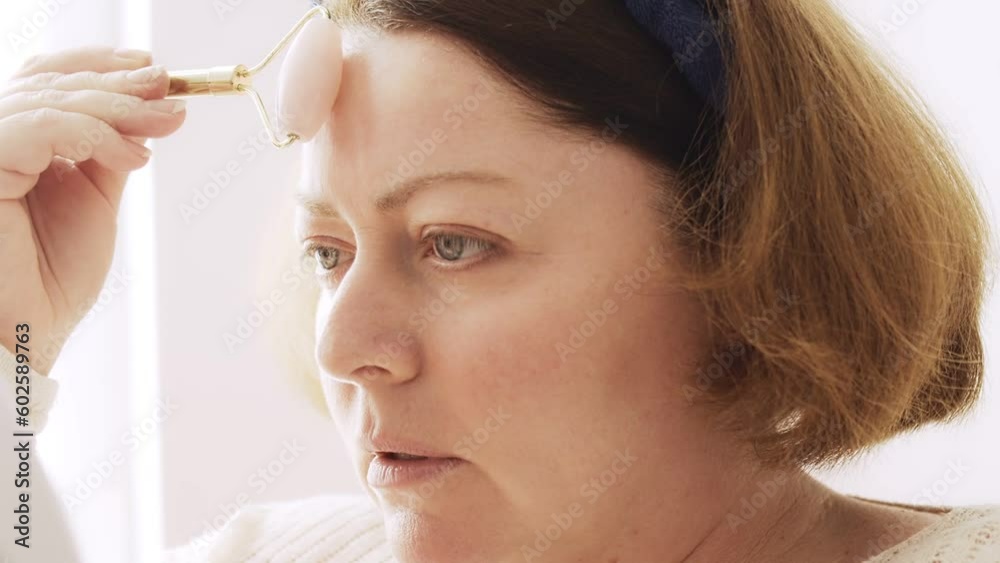 Cosmetic and skin care procedures at home. A middle aged woman massages the skin on her forehead with a roller massager