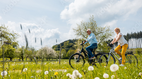 Senior coSenior couple riding bicycles in spring through a meadowuple riding bicycles in spring