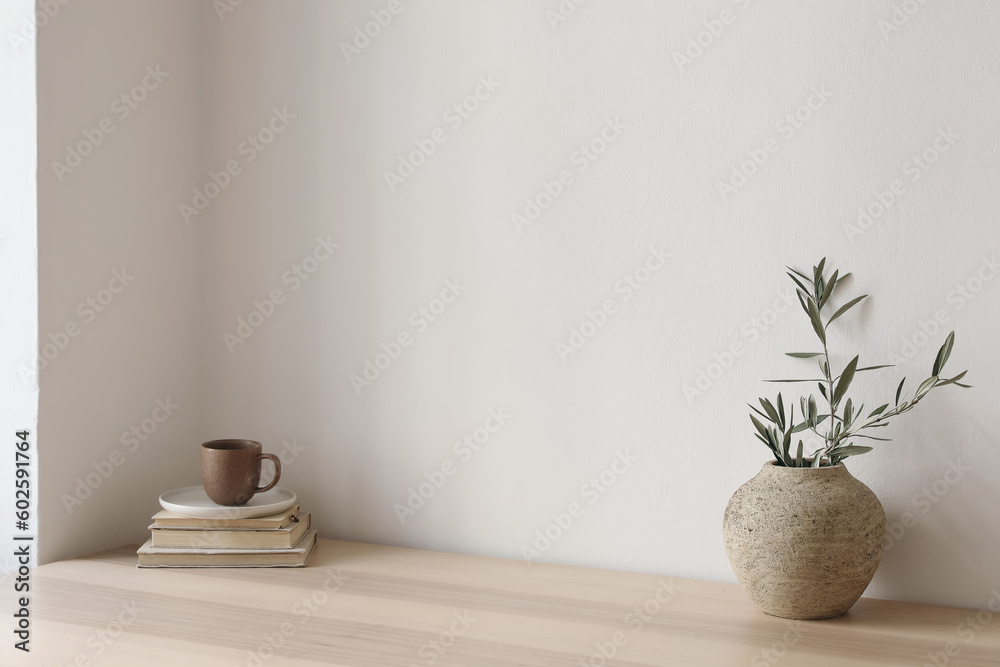 Obraz premium Neutral Mediterranean home design. Textured vase with olive tree branches, cup of coffee. Books on wooden table. Living room still life. Empty wall copy space. Modern interior, no people. Lateral view