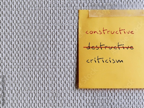 Note stick on copy space office wallpaper with handwritten DESTRUCTIVE CRITICISM, changed to CONSTRUCTIVE CRITICISM - means to shift focus on negative to be on building up other person photo