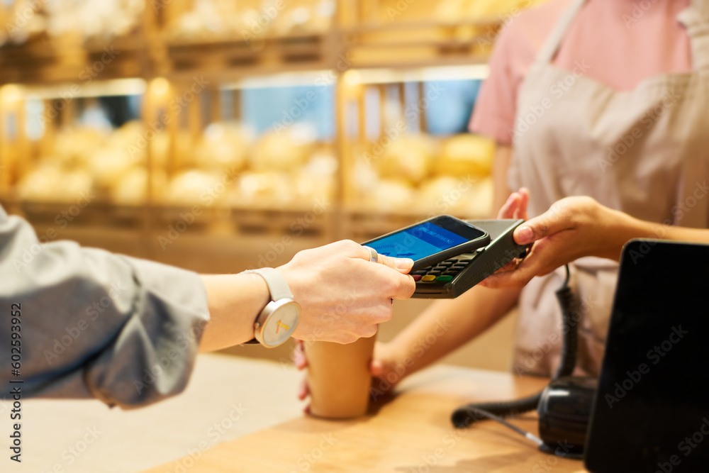 Obraz premium Focus on hands of young clerk and buyer during process of contactless payment over counter desk against display with fresh bread