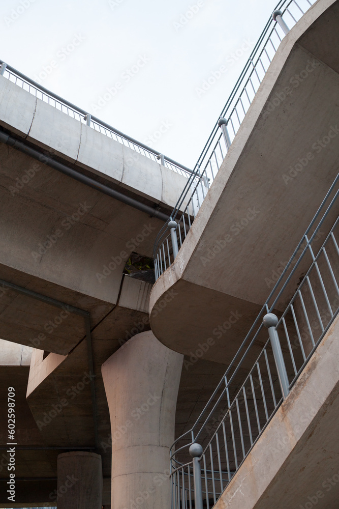 Fototapeta premium Low angle view of a staircase to a modern concrete bridge. Beautiful geometric background with a traffic overpass with grey railing and nobody on it