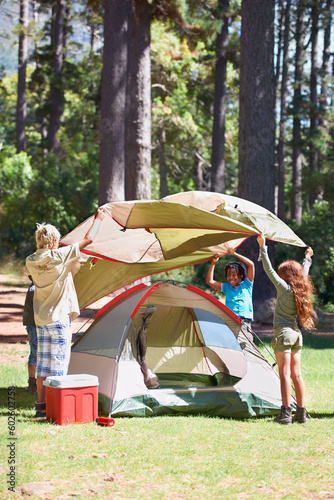 Children, tent and camping setup in forest for shelter, cover together on the grass in nature. Happy kids in teamwork setting up tents for camp adventure or holiday vacation in the woods
