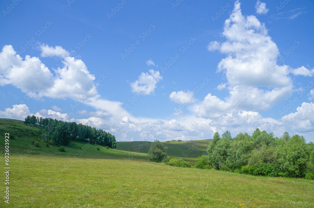 Beautiful clouds in the blue sky bright summer sun illuminates the green meadows on the hills.