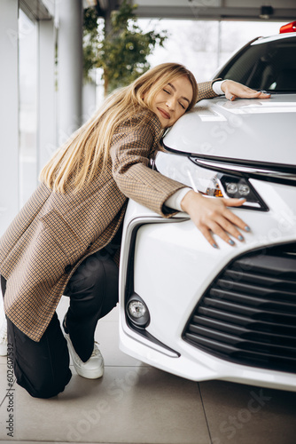 Beautiful woman hugging a car in a car showroom
