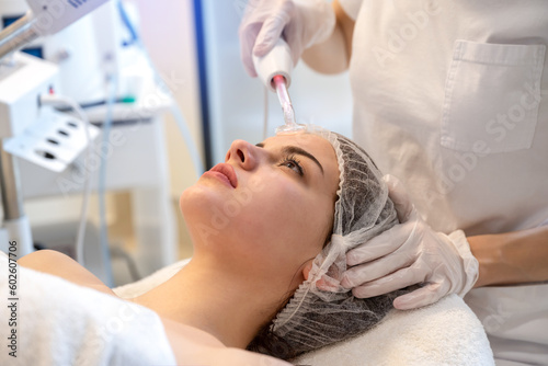 Close up of young woman receiving electric darsonval facial massage after procedure at beauty clinic. photo