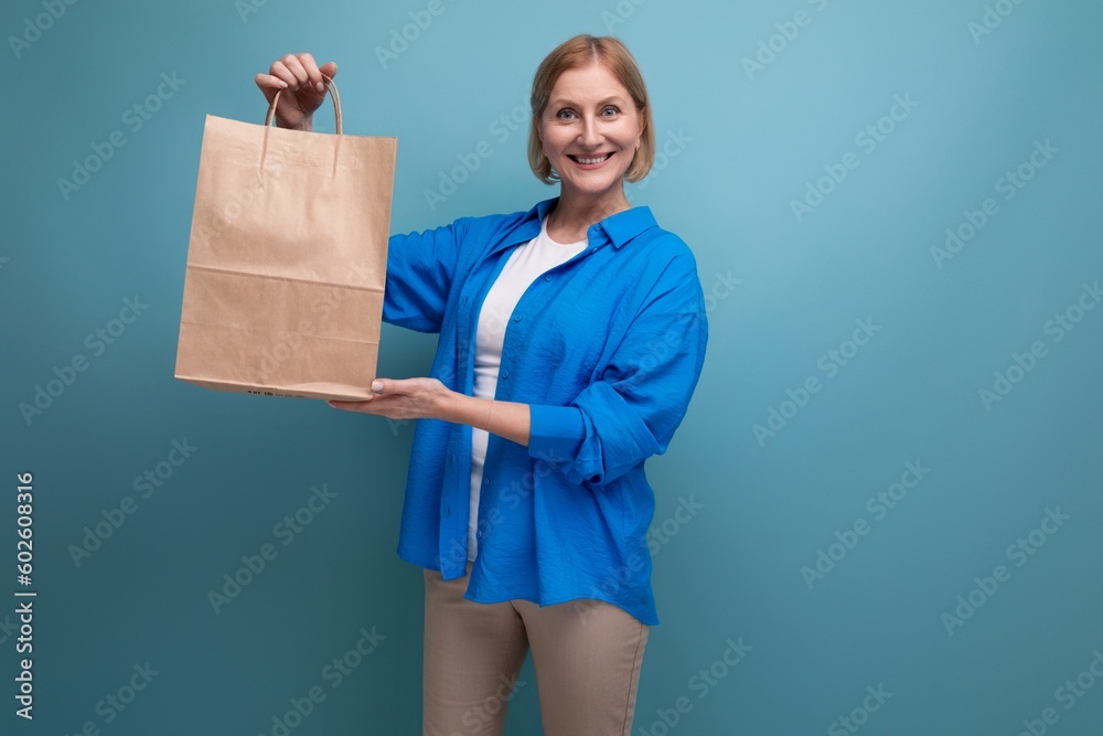 happy mature woman holding craft bag for shopping on blue background copy space happy mature woman holding craft bag for shopping on blue background copy space