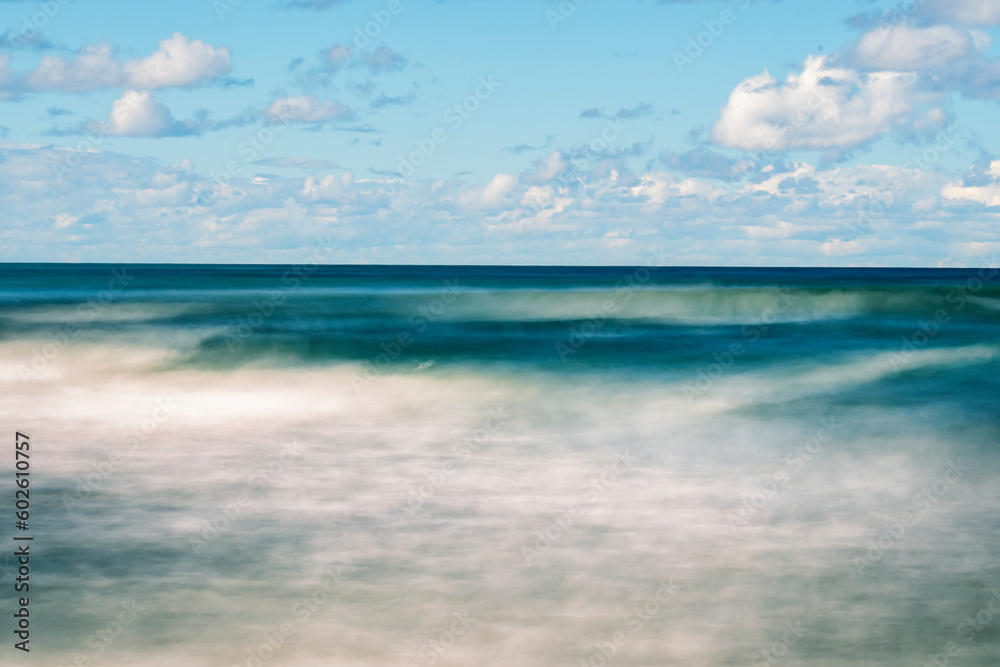 Smooth sea surface with clouds blurred on a long exposure. A seascape in calm summer weather.