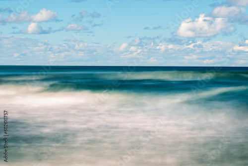 Smooth sea surface with clouds blurred on a long exposure. A seascape in calm summer weather.