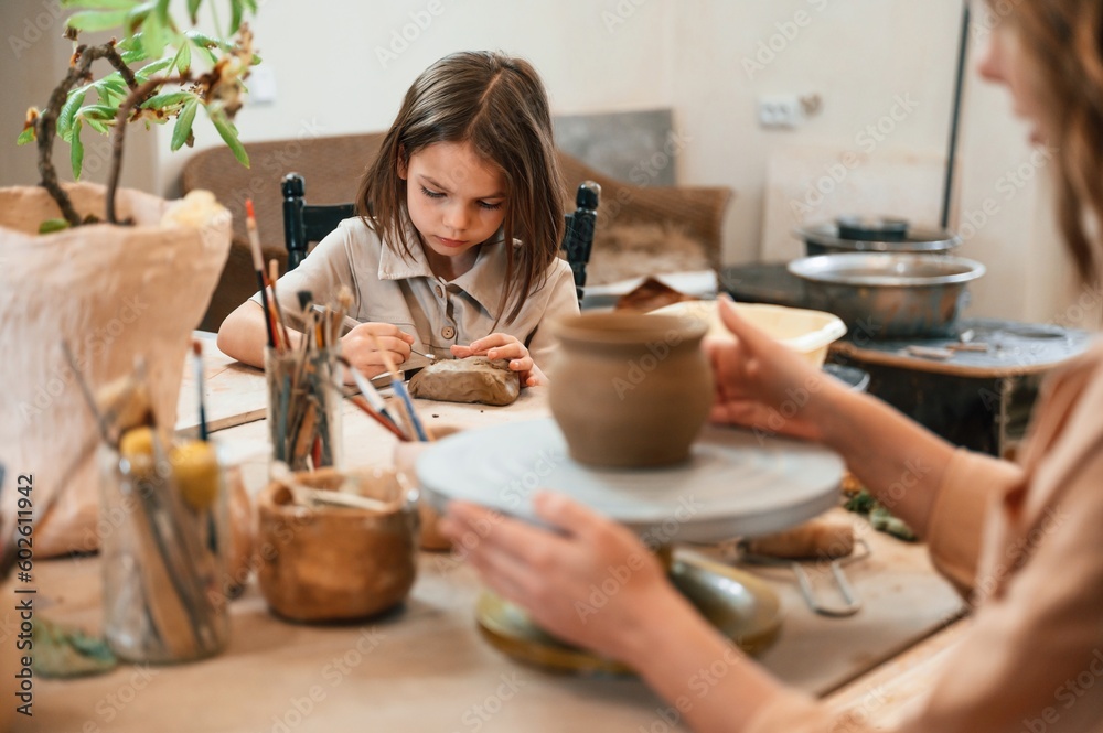 Mother with little girl making ceramic pot in the workshop