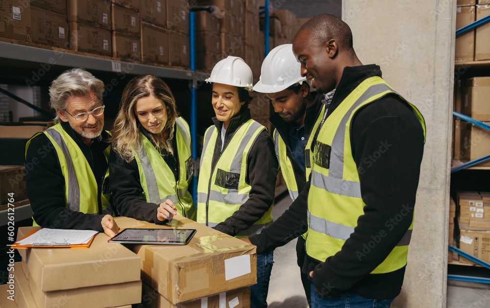 © Jacob Lund - Cheerful warehouse team looking at a statistical report on a digital tablet