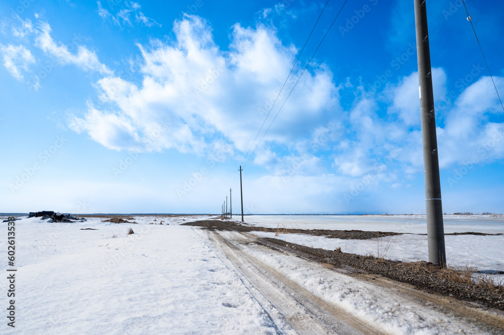 野付半島の雪が積もる大地にて、青い空と大地に通る一本道