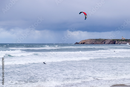 A man kitesurfing on a beach with waves and stormy skies and rough sea