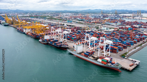 commercial port load and unloading cargo from container ship import and export by crane for distributing goods by trailers transported to customers and dealers, aerial view from drone. © SHUTTER DIN