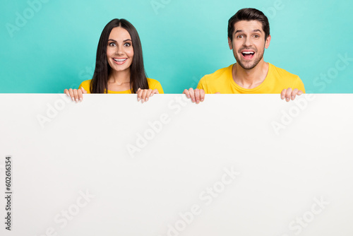 Photo of impressed funny husband wife dressed yellow t-shirts rising poster empty space isolated turquoise color background