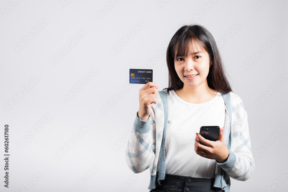 Woman excited smiling hold mobile phone and plastic debit credit bank card for payment studio shot isolated white background, happy young female using smartphone buy and pay online shopping Woman excited smiling hold mobile phone and plastic debit credit bank card for payment studio shot isolated white background, happy young female using smartphone buy and pay online shopping