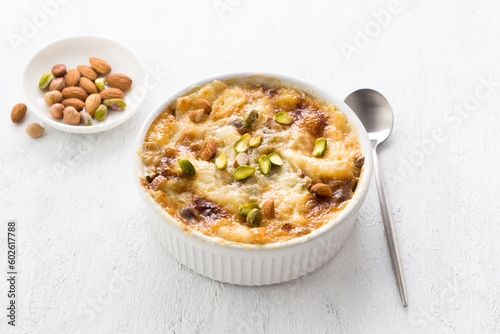 Traditional Arabic dessert Umm Ali in a white ceramic form decorated with nuts on a light gray background