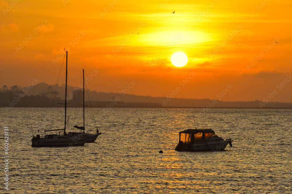 A boat sails as the sun sets, on the beach off the coast in Uruguay, Montevideo with a beautiful golden yellow and orange light