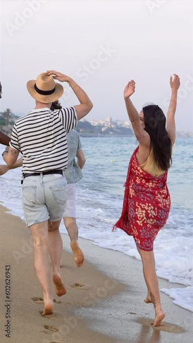 Young friends having fun running on the beach near the sea at sunset. Lifestyle travel holiday vacation in summer - vertical video