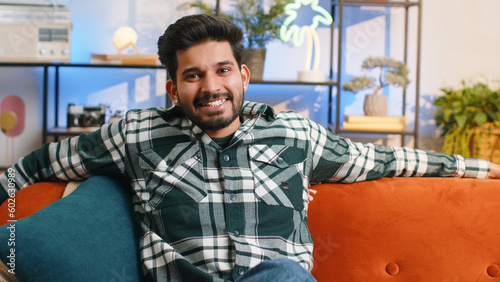 Portrait of happy calm indian man at home couch smiling friendly, glad expression looking away dreaming resting, relaxation feel satisfied concept good news, celebrate win. Hindu guy in living room © Andrii Iemelianenko