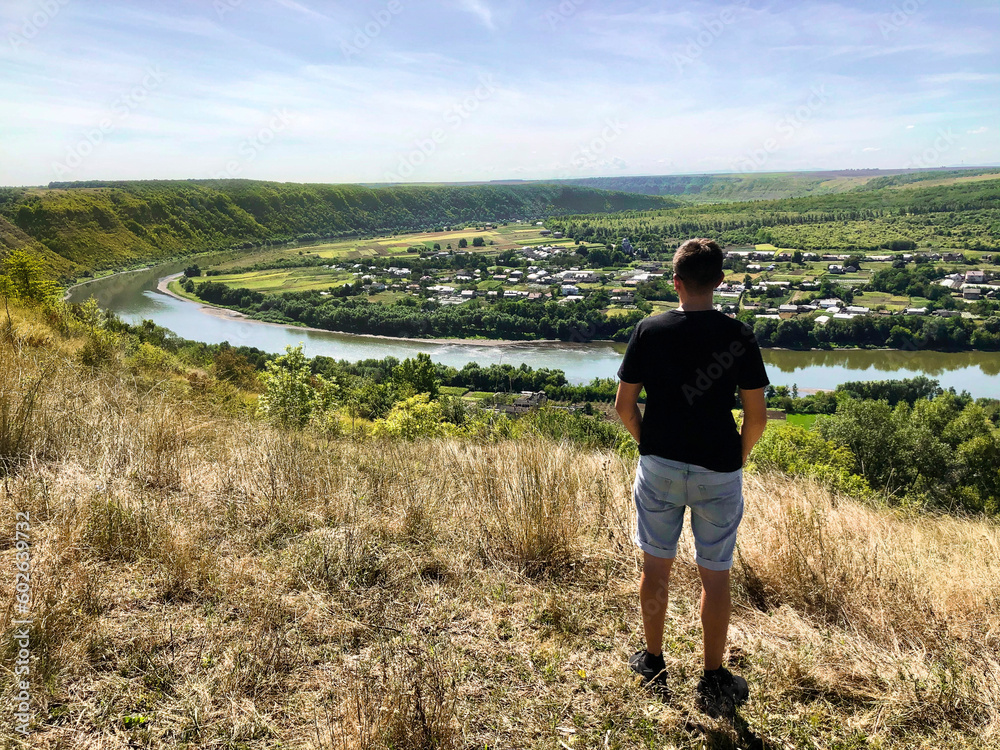A young man stands on a mountain and looks at the beautiful landscape of a mountain canyon. Top view. Dniester Canyon, Ukraine A young man stands on a mountain and looks at the beautiful landscape of a mountain canyon. Top view. Dniester Canyon, Ukraine