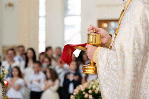 A priest of the Catholic Church stands in front of the parishioners during the festive Holy Liturgy, holding the chalice with the sacraments in his hands. First Confession and solemn Holy Communion