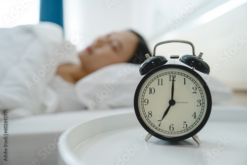 Asian woman resting in bed with alarm clock