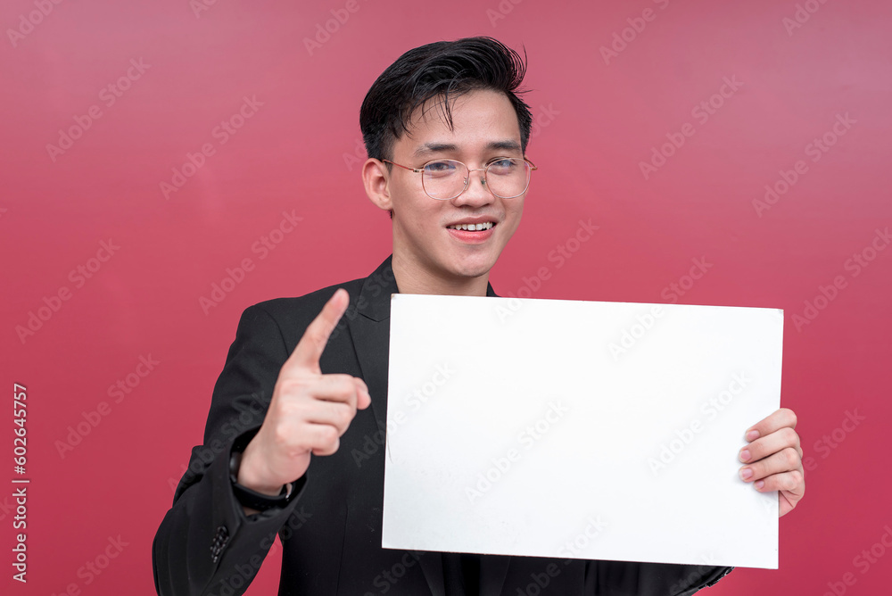Portrait of a smiling young man with glasses holding a placard while pointing upwards. Isolated on a red background. Portrait of a smiling young man with glasses holding a placard while pointing upwards. Isolated on a red background.