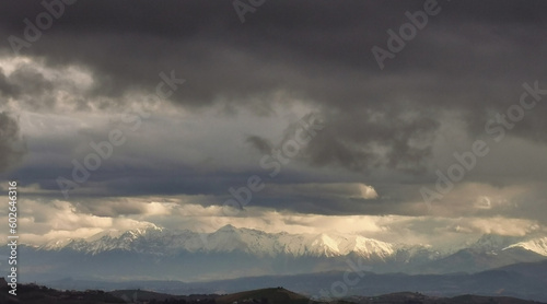 Montagne innevate illuminate dal sole squarciano le nuvole nere prima della tempesta photo
