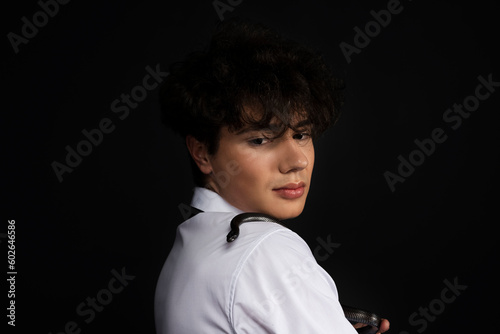 Young handsome man in white shirt with a black snake crawling on his shoulder. Isolated on black background.