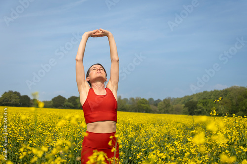 fit, sporty woman runner doing an arm stretch in a yellow field with a blue sky