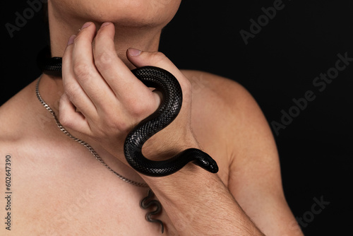 Young handsome man with naked torso, with a black snake crawling around his neck. Isolated on black background. photo