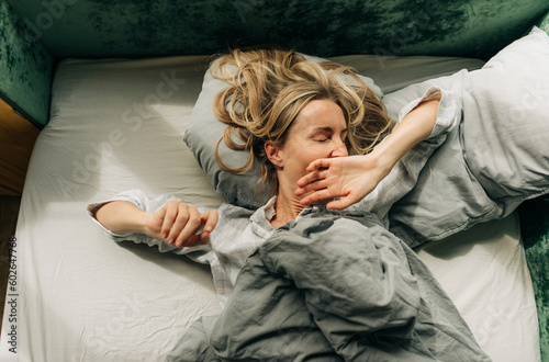 A woman after waking up stretches and yawns lying in bed in the morning. photo